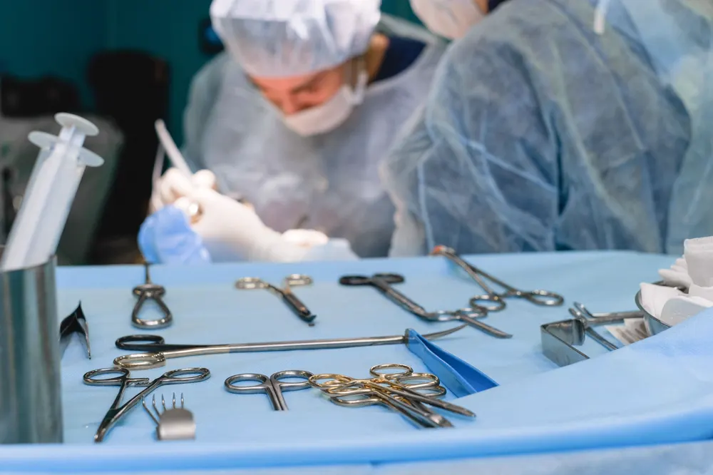 Fotografía de stock: instrumental quirúrgico esterilizado sobre un paño azul, con personal sanitario de fondo.